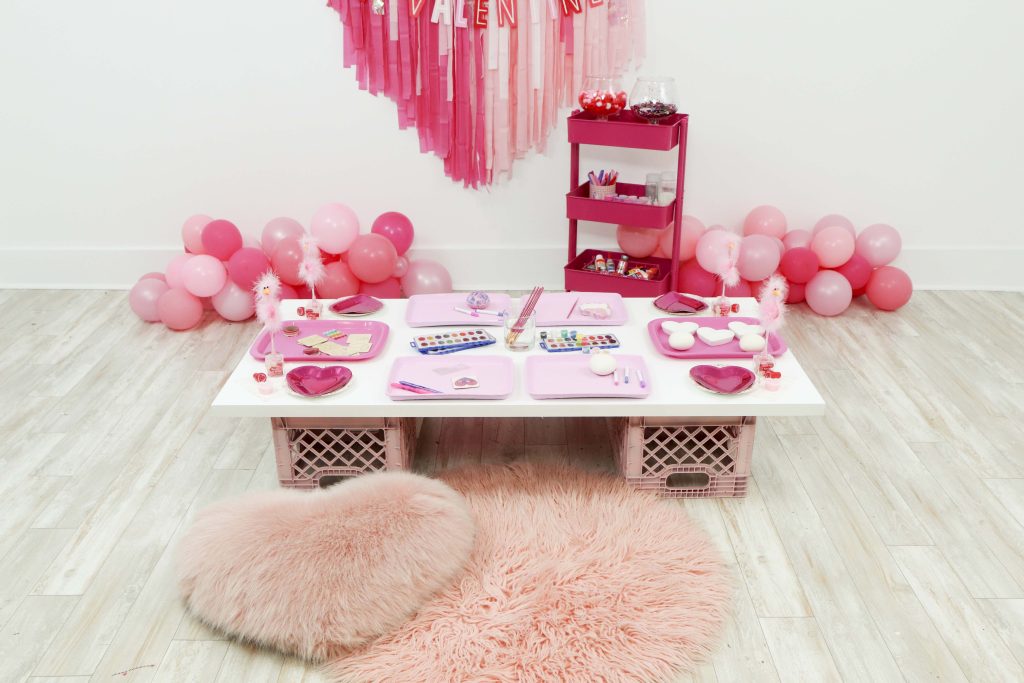 Valentine's craft table for a Valentine's Day Craft Party for Kids with fringe heart backdrop, craft cart, and craft table ideas! Get all of the details now at fernandmaple.com!