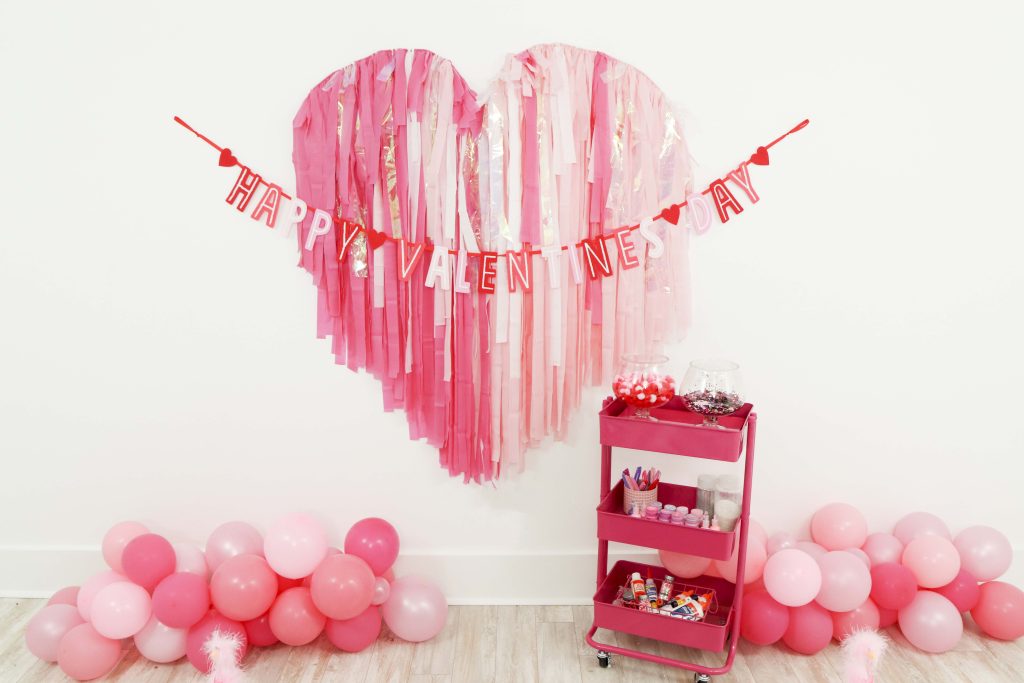 Valentine's backdrop and garland for a Valentine's Day Craft Party for Kids with fringe heart backdrop, craft cart, and craft table ideas! Get all of the details now at fernandmaple.com!