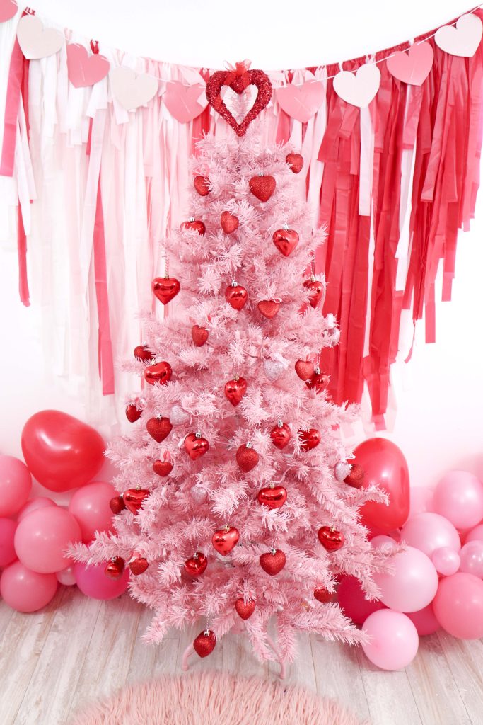 Valentine's Day pink decorated tree- decorate a Valentine's Day tree at a tree decorating party with fun backdrop, decor, and candy heart ornament craft! Get details now at fernandmaple.com.