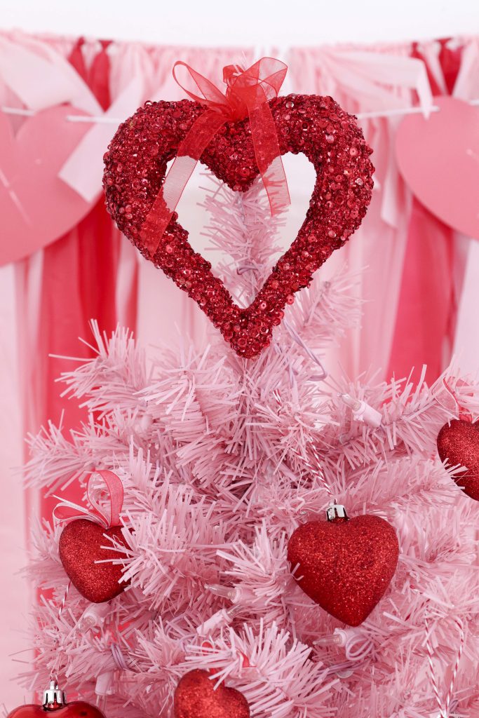 Valentine's Day tree topper- decorate a Valentine's Day tree at a tree decorating party with fun backdrop, decor, and candy heart ornament craft! Get details now at fernandmaple.com.