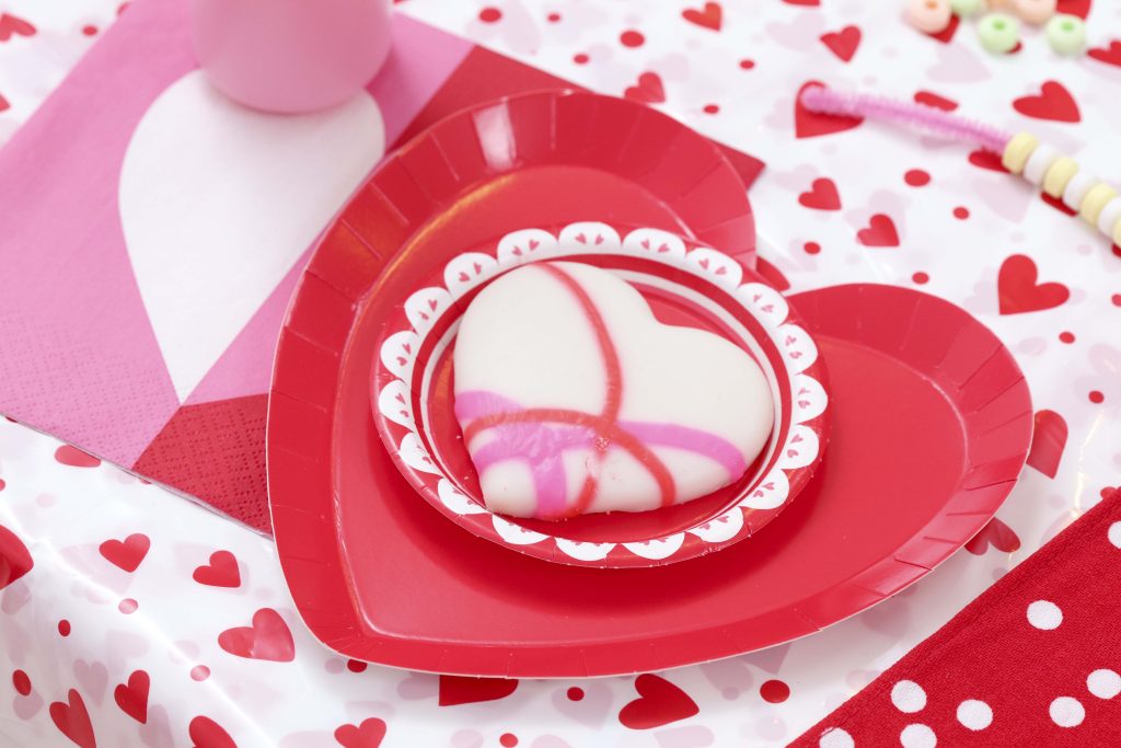 Valentine's Day kid's party place setting - decorate a Valentine's Day tree at a tree decorating party with fun backdrop, decor, and candy heart ornament craft! Get details now at fernandmaple.com.
