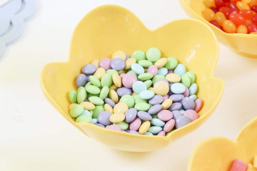 Yellow flower bowl full of Spring candy for a Spring Gingerbread House decorating party - get more Spring Party inspiration now at fernandmaple.com!