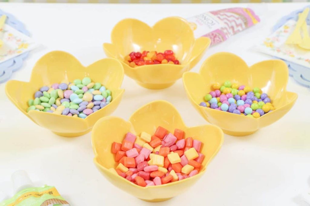 Candies in pastel yellow flower bowls for a Spring Gingerbread House decorating party - get more Spring Party inspiration now at fernandmaple.com!