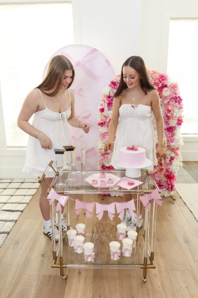 DIY pink floral arch backdrop for graduation party with personalized grad sign as backdrop for cake table and celebratory drinks