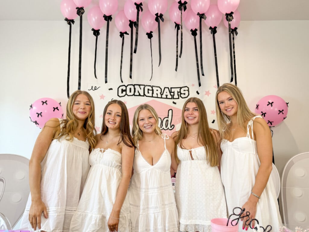 pink Congrats Grad sign framed by pink balloon columns and ceiling balloons with black ribbon tails and bows at graduation party