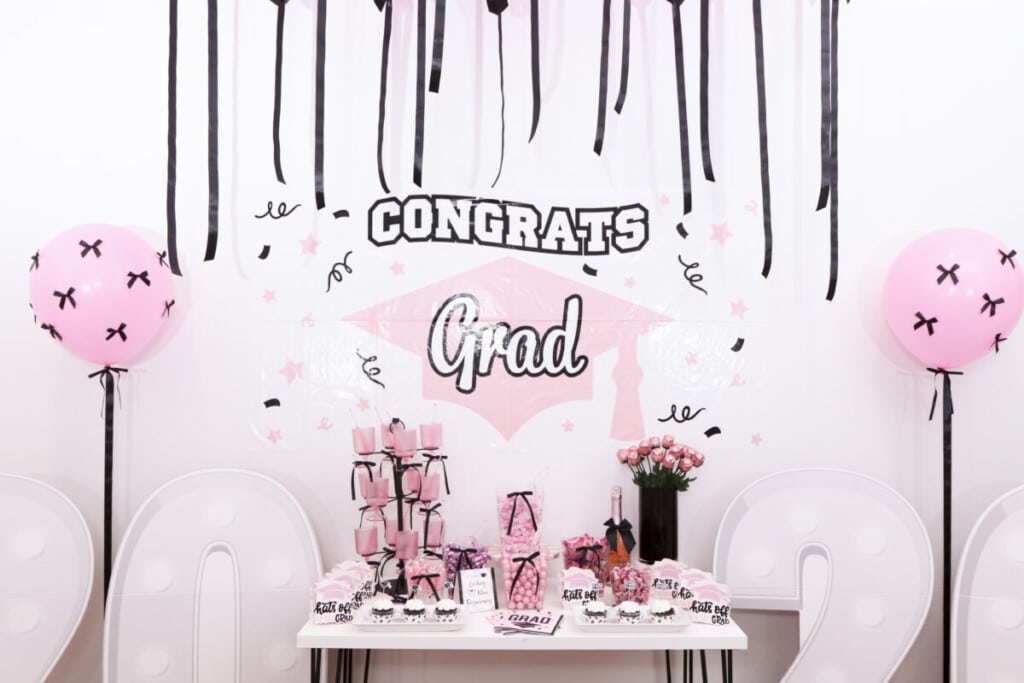pink and black graduation party candy bar in front of Congrats Grad sign backdrop with balloon columns 