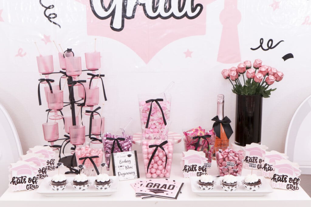 pink and black graduation party candy bar showing height variation from glass tower to candy vessels to cupcakes
