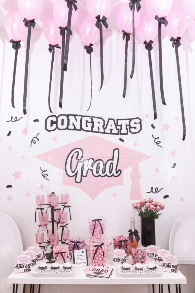 pink Congrats Grad sign framed by pink  ceiling balloons with black ribbon tails and bows at graduation party