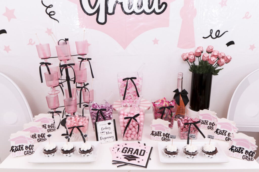 pink and black graduation party candy bar with personalized ribbon and signage in front of statement backdrop