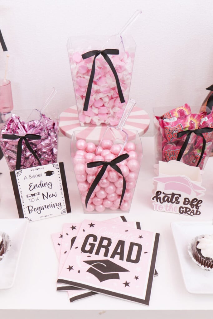 clear candy vessels filled with pink gumballs, taffy and caramels with black bows at graduation party candy bar