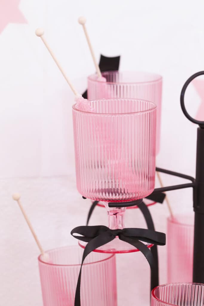 pink ribbed glasses on black candelabra tower stand with black bows and candy sticks at graduation party candy bar