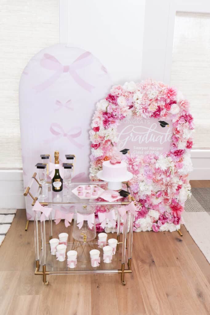 pink and black graduation party setup with floral arch backdrop