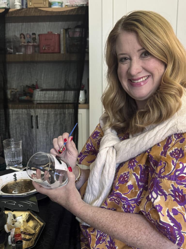 Applying a base coat of paint to a wine glass at a gothic paint and sip party