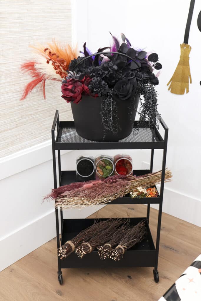 black three-tier craft cart with dramatic dark floral arrangement and broom making supplies at witch party