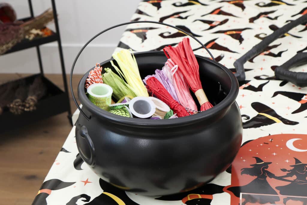 DIY broom making supplies in a cauldron including jute, leahter cord and sequins