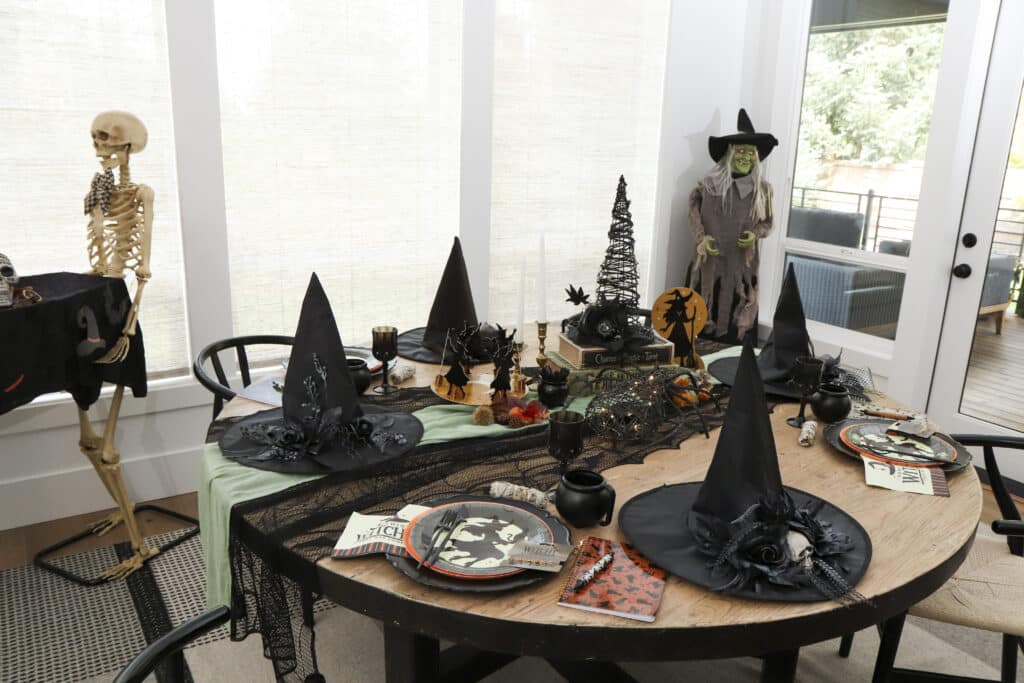 Practical Magic party ideas — witch party table setting with witch plates, black cauldron mugs, decorated witch hats and spell book centrepiece