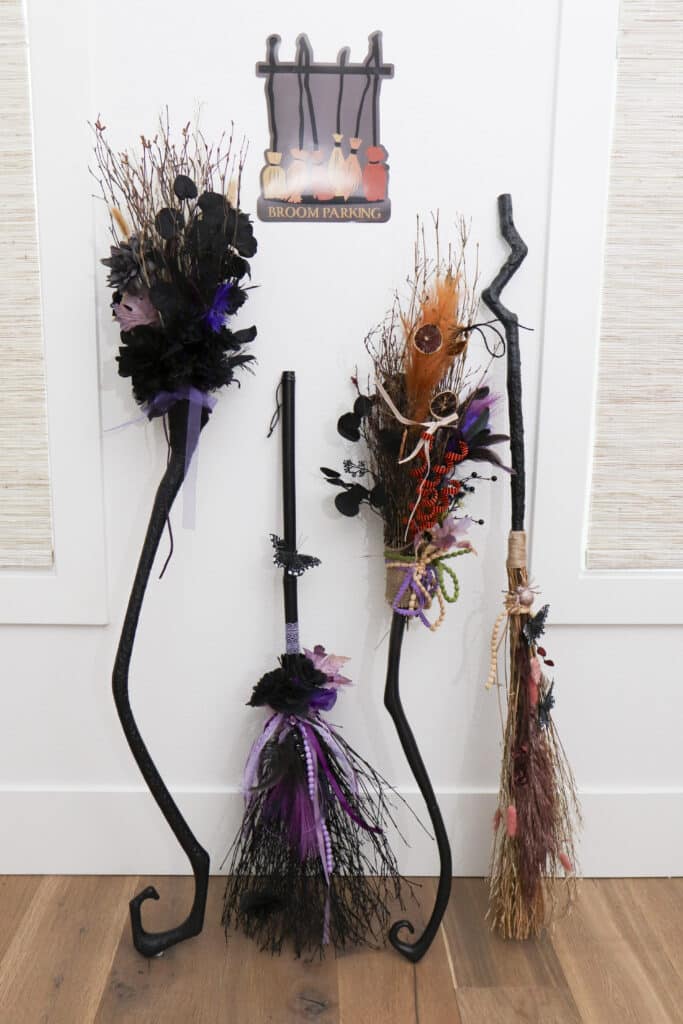 four handmade decorated witch brooms under Broom Parking sign at witch party